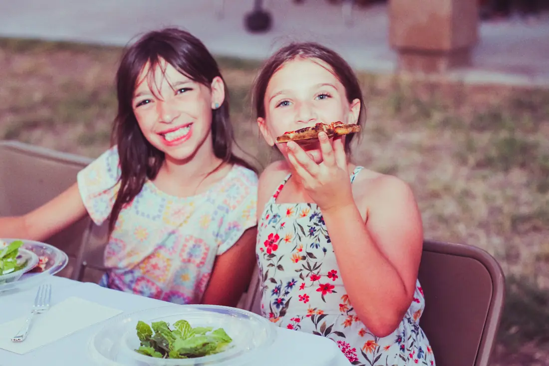 Young guests grinning over slices of wood-fired pizza