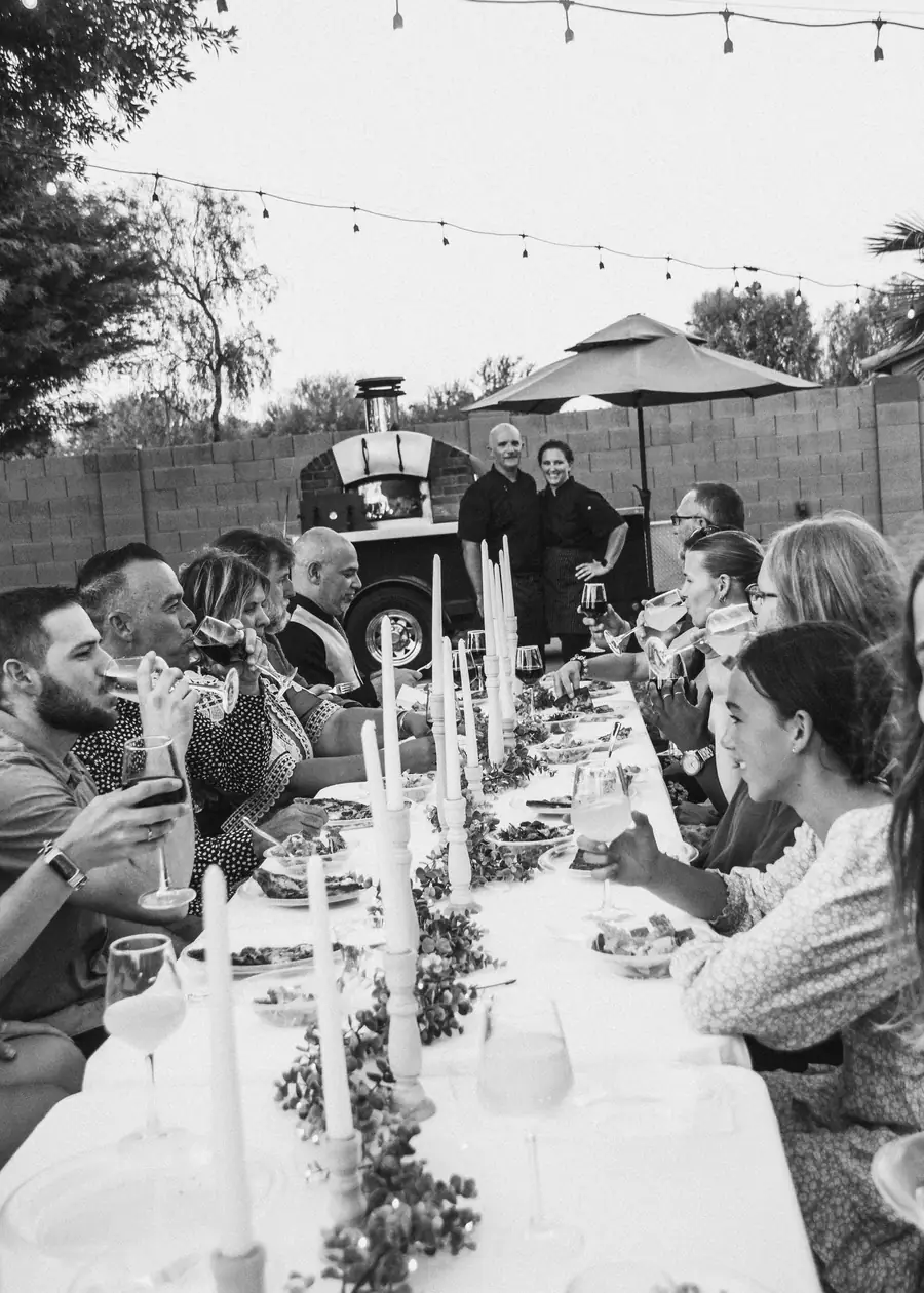 Candlelit long-table dinner with guests and the wood-fired oven