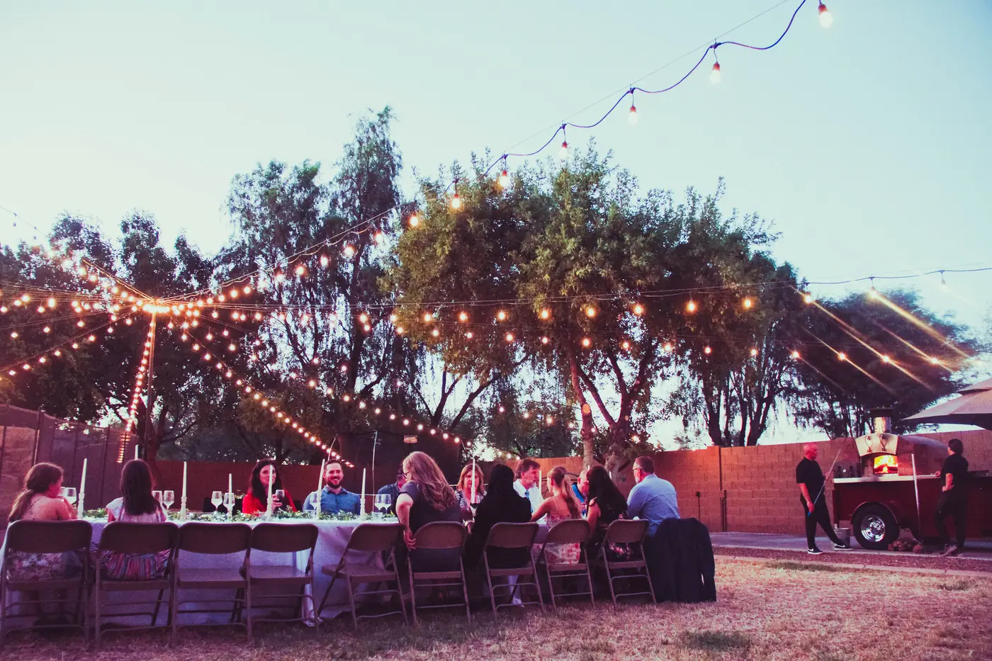 Guests dining under string lights with the wood-fired oven glowing