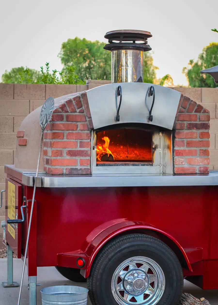 The mobile wood-fired oven burning on its red trailer